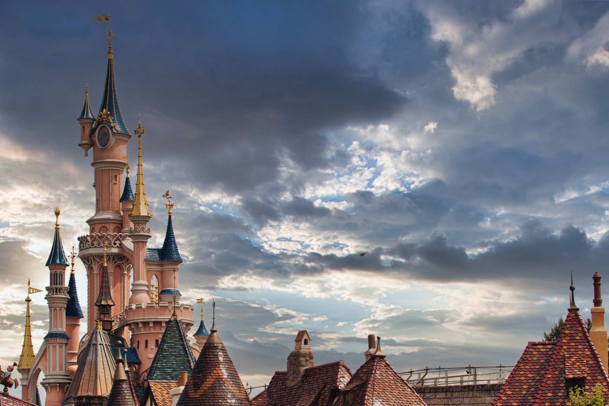 Fairytale Castle with Towers and Tiled Roofs under Cloudy Sky at Disneyland Paris, France.