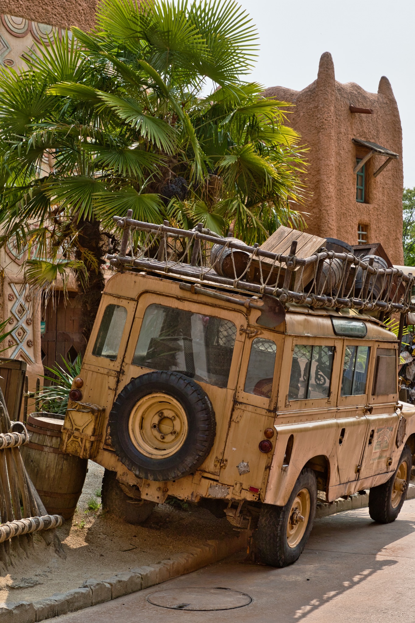 Parked Tan SUV with Roof Load Near Palm Tree and Earthen Building at Disneyland Paris, France.