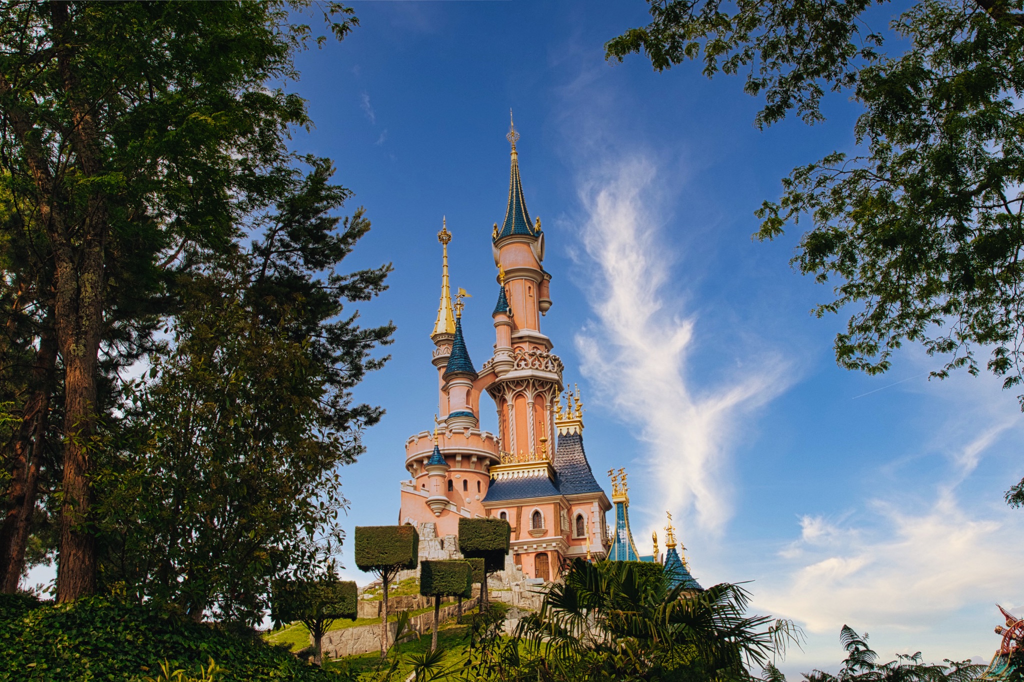 Pink Castle with Blue Roofs Framed by Trees Under Blue Sky at Disneyland Paris, France.