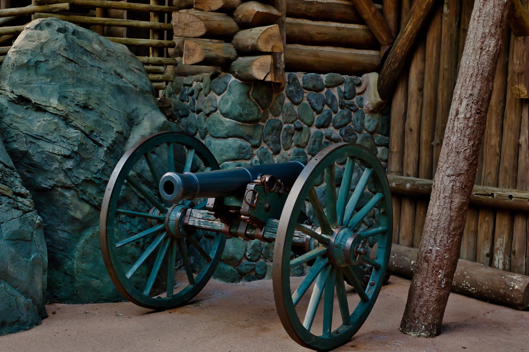 Cannon with Green Wheels in Front of Stone and Log Structures at Disneyland Paris, France.
